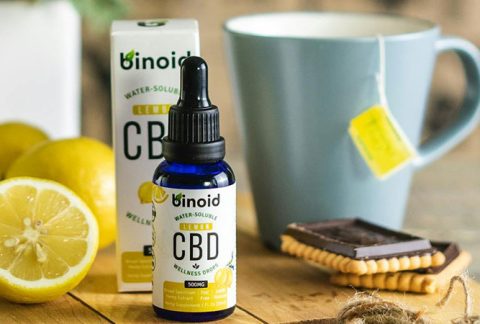 a small bottle of CBD oil beside sliced lemons and a cup of tea on top of a chopping board