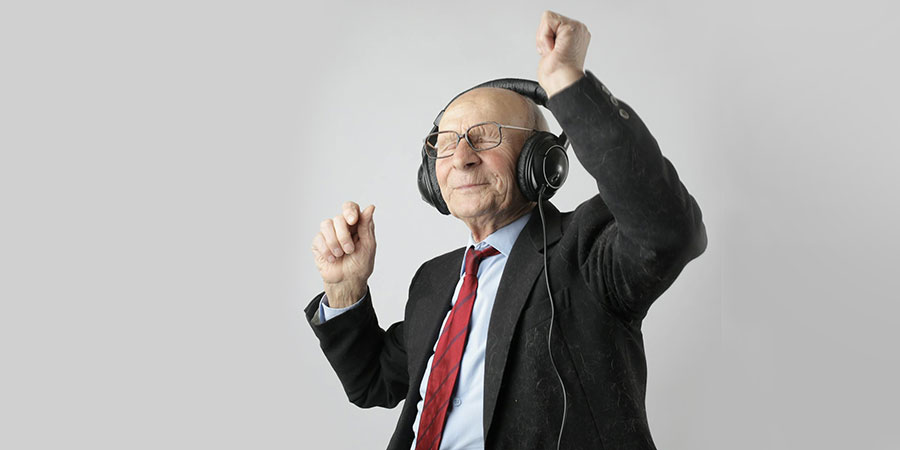 an elderly man wearing a black suit while enjoying listening to music with his headphones
